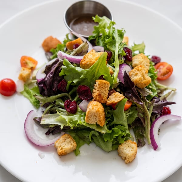 Mixed green salad with croutons, red onions, cherry tomatoes, dried cranberries, and dressing.
