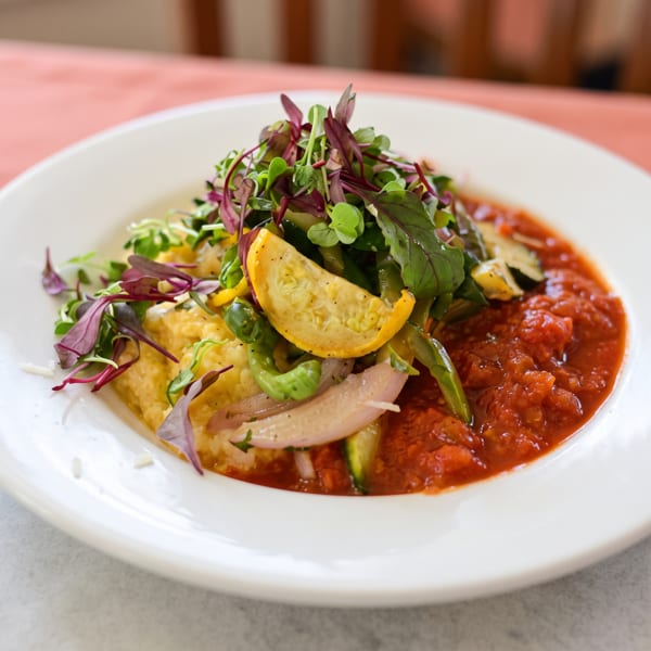 Polenta with red sauce, topped with microgreens, yellow squash, red onion, and green peppers.
